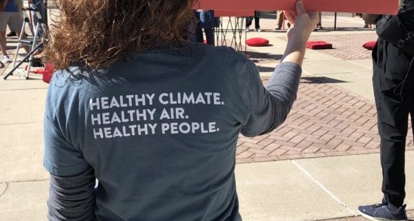 A photo from a previous NCUC carbon plan hearing shows a woman holding a sign that says "no more fossil fuels amen"